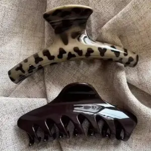 Zwei große Haarklammern, eine mit Leopardenmuster und eine in Dunkelbraun, auf grobem Stoff