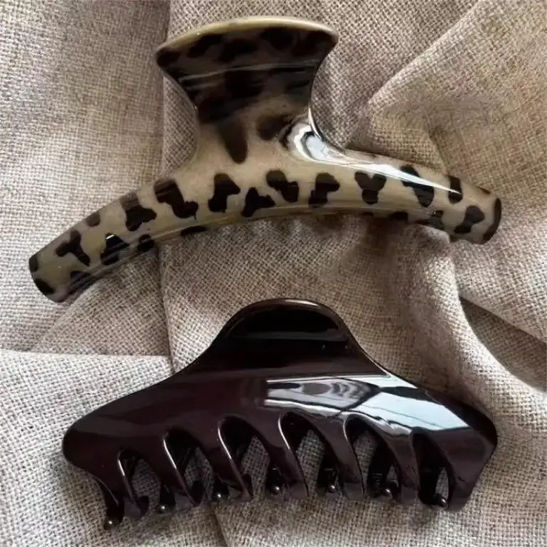 Zwei große Haarklammern, eine mit Leopardenmuster und eine in Dunkelbraun, auf grobem Stoff