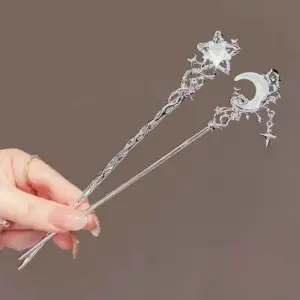 Zwei silberfarbene Haarnadeln mit Mond und Stern in einer Hand gehalten