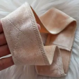 Beiges breites Haarband mit weich wirkender Oberfläche in der Hand gehalten